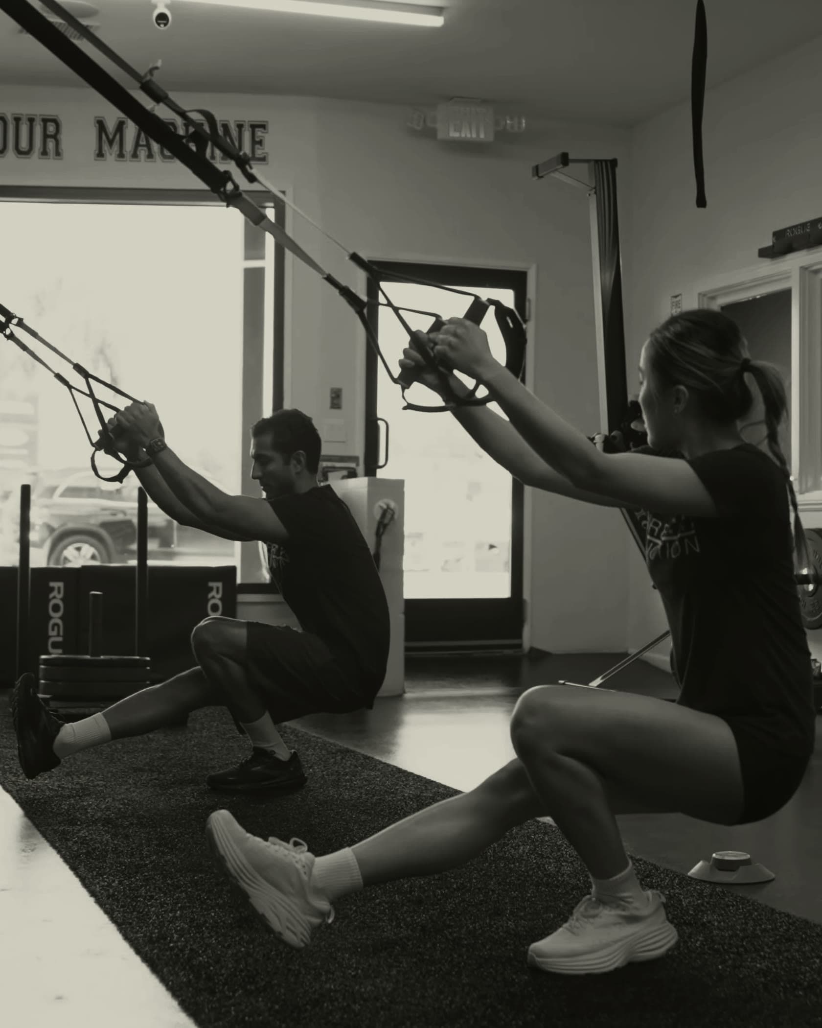 Two clients holding matching TRX single leg squats side by side at Pure Function